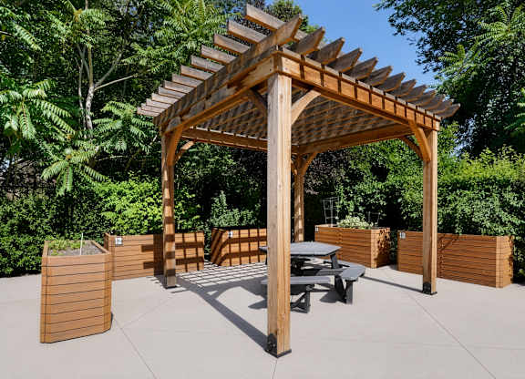 A wooden pergola with a table and chairs is set up in a garden.