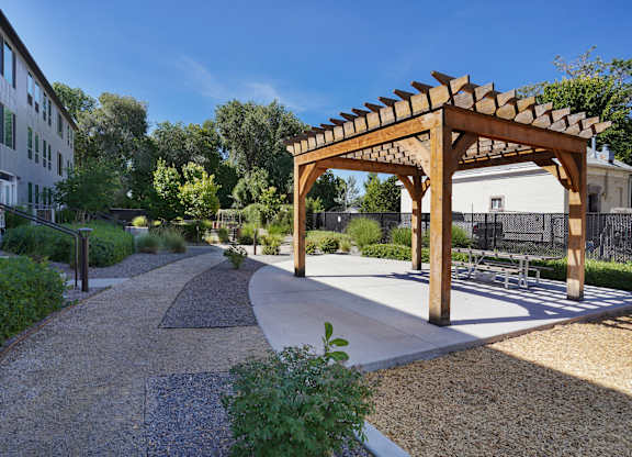 A wooden pergola is situated in the middle of a gravel path.