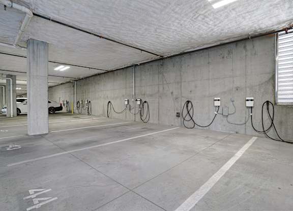 A parking garage with concrete walls and floors, and several parking spots with charging stations.