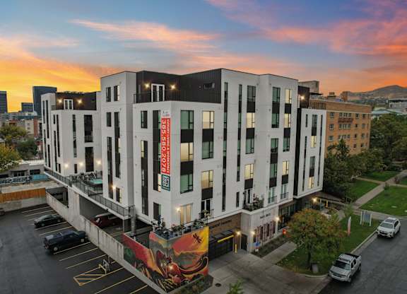 A modern building with a mural on the side is surrounded by a parking lot.