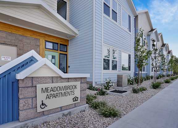 A sign for Meadowbrook Apartments is displayed in front of a building.