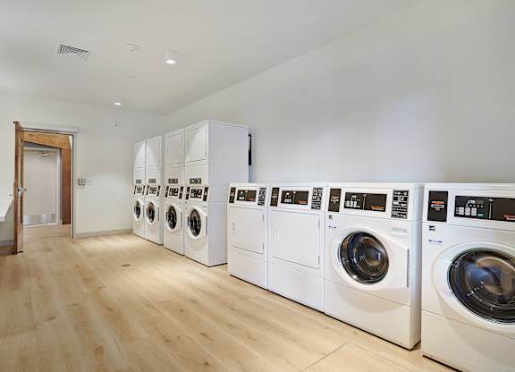 A row of white front load washing machines in a laundry room.