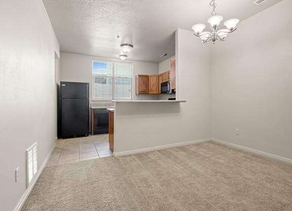 A room with a black fridge and a carpeted floor.