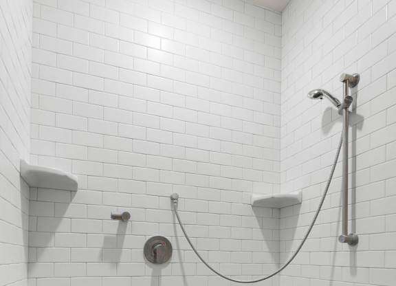 a white tiled bathroom with two urinals and a hose