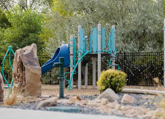 A playground with a blue slide and a black fence.