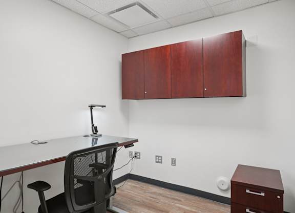 A white desk with a black chair and a white table top with a black base and a black lamp on it.
