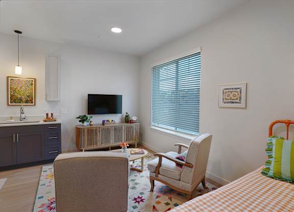 A living room with a television, two chairs, a couch, and a painting on the wall.