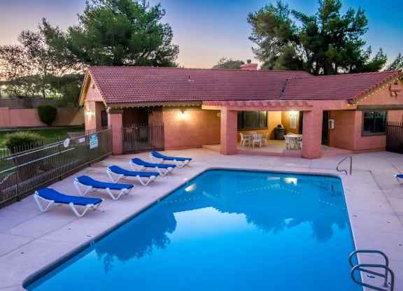 a swimming pool in front of a house with blue chairs