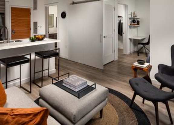 A modern living room with a grey ottoman and a black chair.