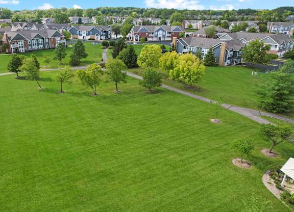 A large grassy field with trees and houses in the background.