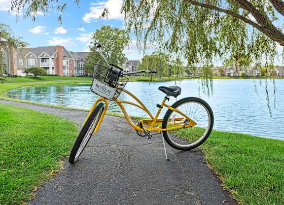 A yellow bicycle with a basket is parked by a lake.