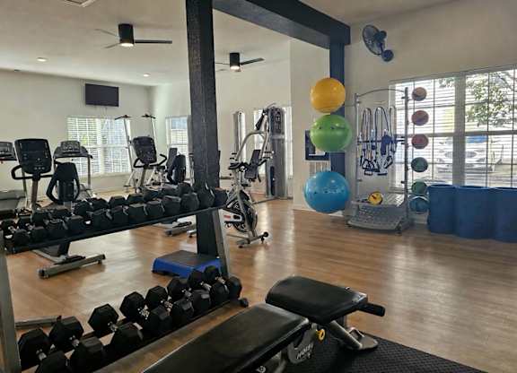 A gym with a variety of equipment including dumbbells, weight machines, and a bench press.