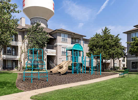 A playground with a slide and swings in front of a building.