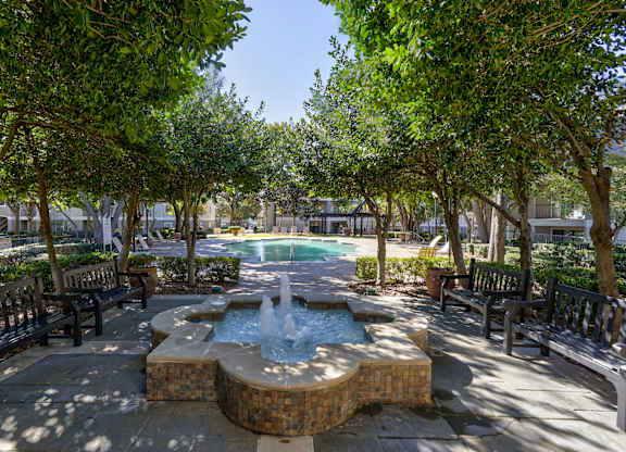 A fountain in the middle of a park surrounded by benches and trees.