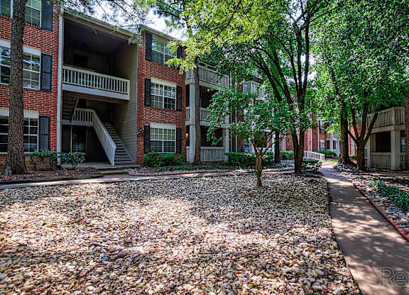 A courtyard with a gravel ground and trees in front of a red brick building.