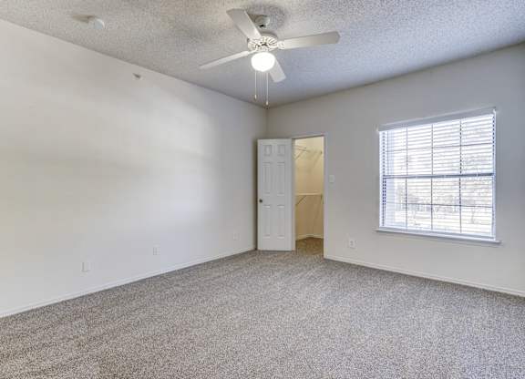 Spacious bedroom at Saxony at Chase Oaks Apartments in Dallas, TX, with white walls, neutral carpet, a ceiling fan, and a walk-in closet.