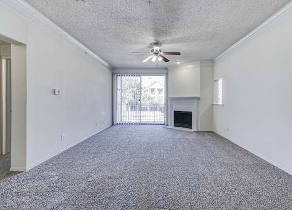 A bright living room at Saxony at Chase Oaks Apartments in Dallas, TX, with a fireplace, built-in fireplace mantel, a ceiling fan, and carpeted floors, with ample natural light streaming through large windows.