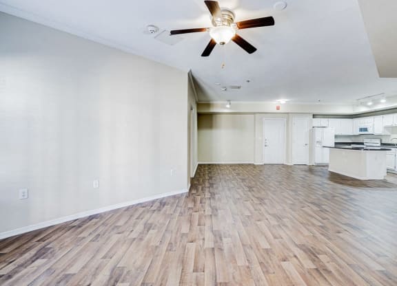 an empty living room with a ceiling fan and a kitchen