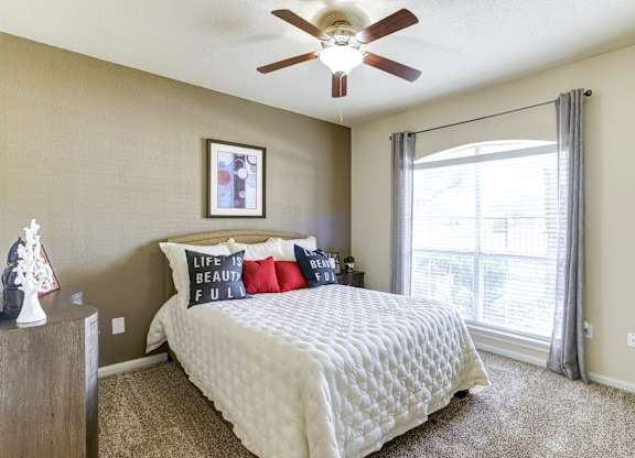A bedroom with a bed, pillows, a ceiling fan, and a window with curtains.