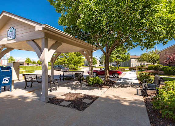 A covered outdoor seating area with a mailbox and a tree at Prairie Commons - 55+ Senior Community Apartments, Lawrence, KS, 66049
