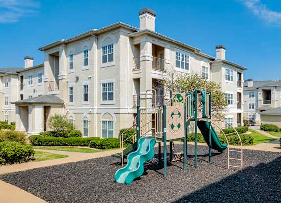 A playground with a green slide in front of a large building.