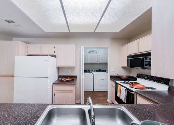 A kitchen with a white fridge and a stainless steel sink.