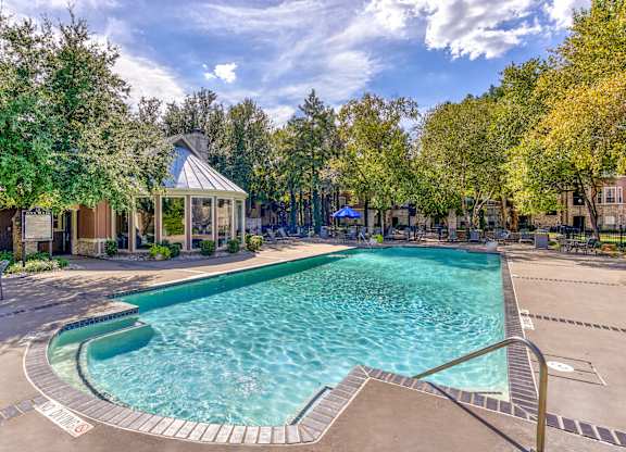A large outdoor swimming pool surrounded by trees and a gazebo.