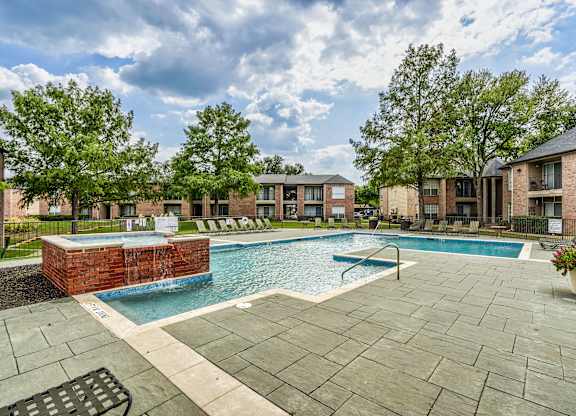 A swimming pool surrounded by a brick wall and a patio area with a bench.
