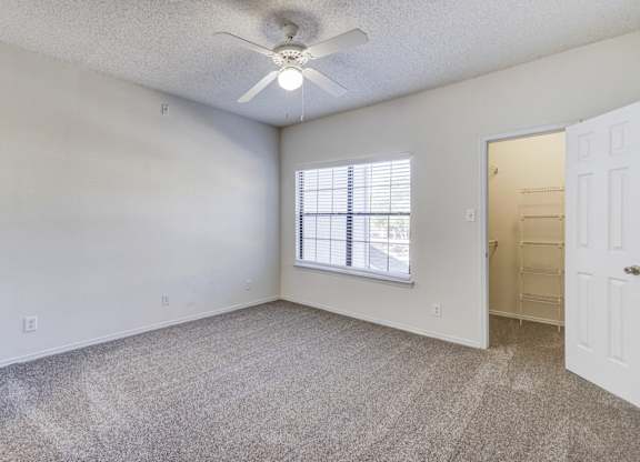 Bedroom at Saxony at Chase Oaks Apartments in Dallas, TX, with white walls, neutral carpeting, a ceiling fan, and a walk-in closet.