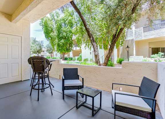 A patio with a chair, table and a view of a tree and building.