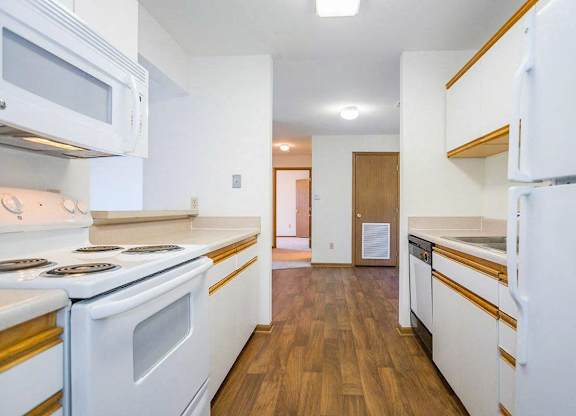 A kitchen with white appliances and wooden floors at Prairie Commons - 55+ Senior Community Apartments, Kansas