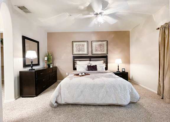 A bedroom with a large bed, a dresser, and a ceiling fan.
