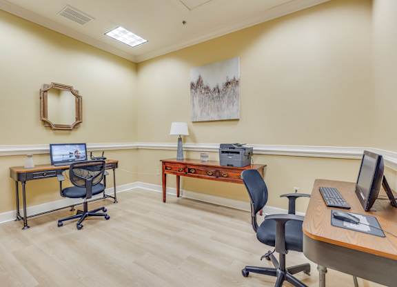 A room with two desks and chairs, one with a laptop and the other with a desktop computer.