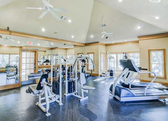 Fully equipped fitness center at Saxony at Chase Oaks Apartments in Dallas, TX, featuring treadmills, weight machines, and mirrored walls in a well-lit space with ceiling fans.