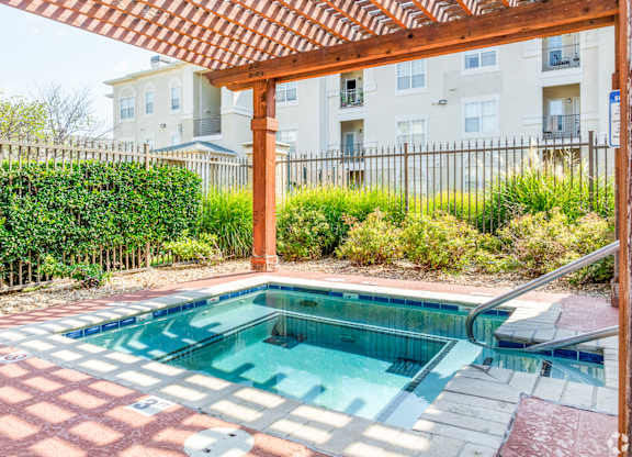 A small pool with a red tile border and a wooden pergola over it.