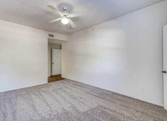 Large primary bedroom at Saxony at Chase Oaks Apartments in Dallas, TX, featuring a ceiling fan, walk-in closet, and natural light through large windows.