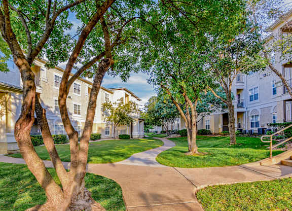 A tree-lined walkway leads to apartment buildings.