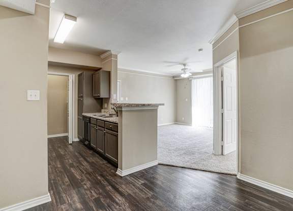 Open layout view of the kitchen and living area at Saxony at Chase Oaks Apartments in Dallas, TX, showcasing wood-style flooring, crown molding, and modern cabinetry.