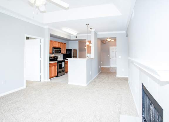 A spacious living room with a fireplace and a kitchen in the background.