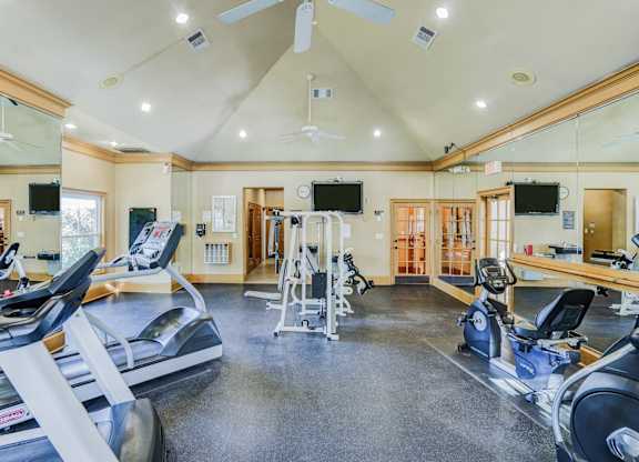 Modern fitness center at Saxony at Chase Oaks Apartments in Dallas, TX, equipped with treadmills, exercise bikes, strength-training machines, and wall-mounted TVs in a bright, spacious room with vaulted ceilings and large mirrors.