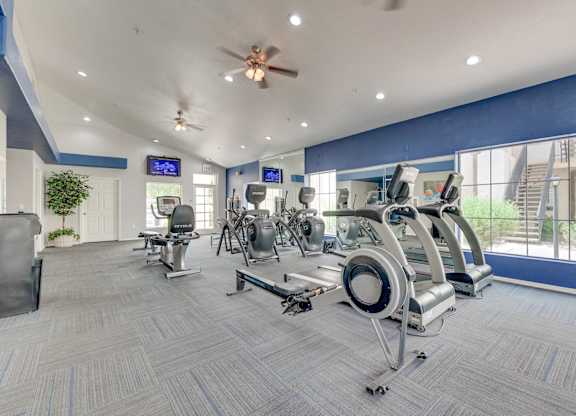 A gym with a variety of exercise equipment and a ceiling fan.