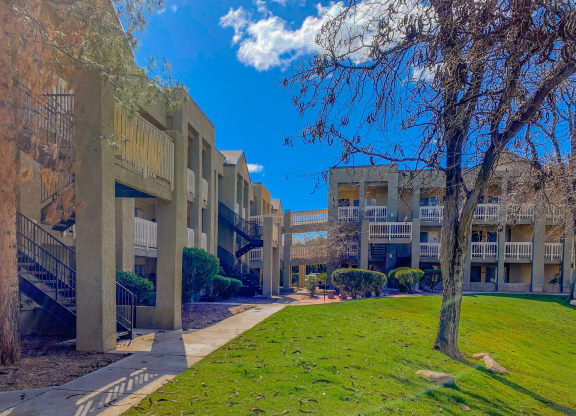 a row of apartment buildings with a green lawn and trees
