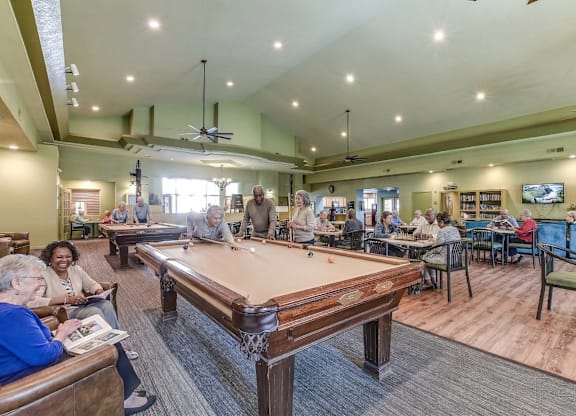 A group of people playing pool in a room with a pool table.