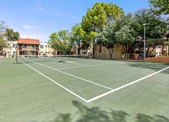 A tennis court surrounded by trees and buildings.