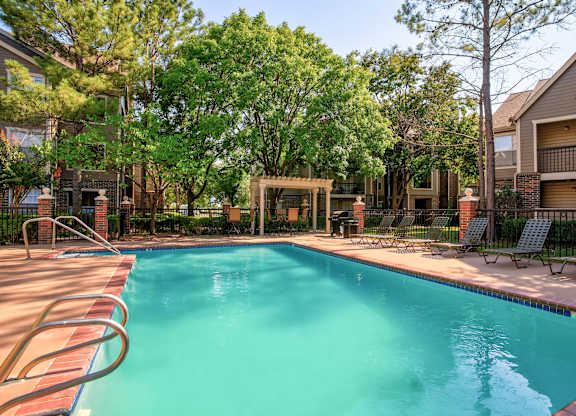 A swimming pool surrounded by trees and chairs.