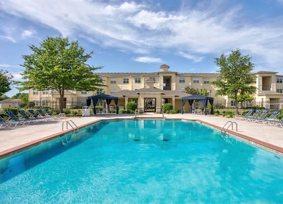 A large swimming pool in front of a building with a blue sky and clouds in the background.