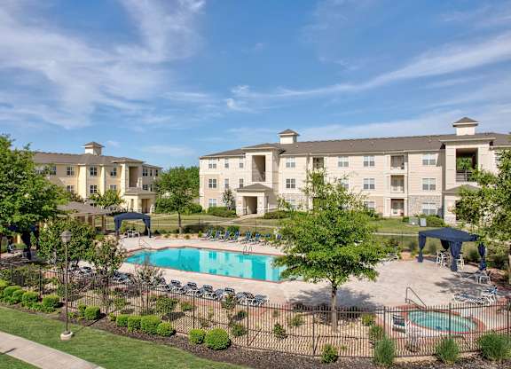 A large apartment complex with a pool and a fenced in area with trees.