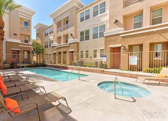 A pool area with sun loungers and a fence in front of apartment buildings.