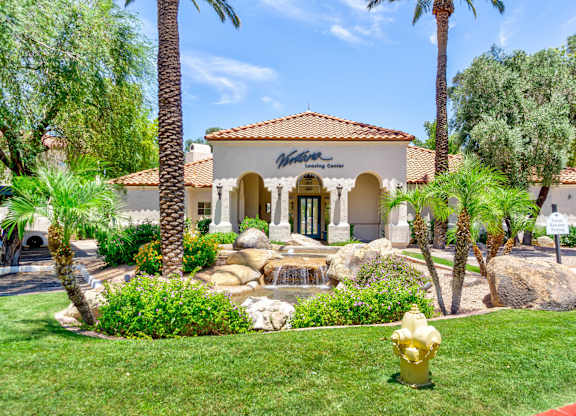 A building with a red tile roof and a sign that says "Winston's Club" is surrounded by palm trees and a garden with a waterfall.