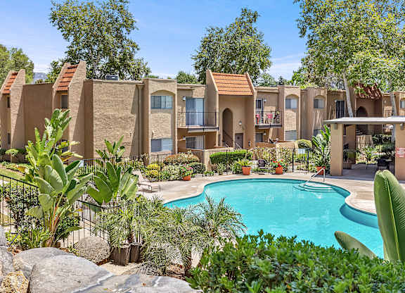 A pool surrounded by plants and a building in the background.